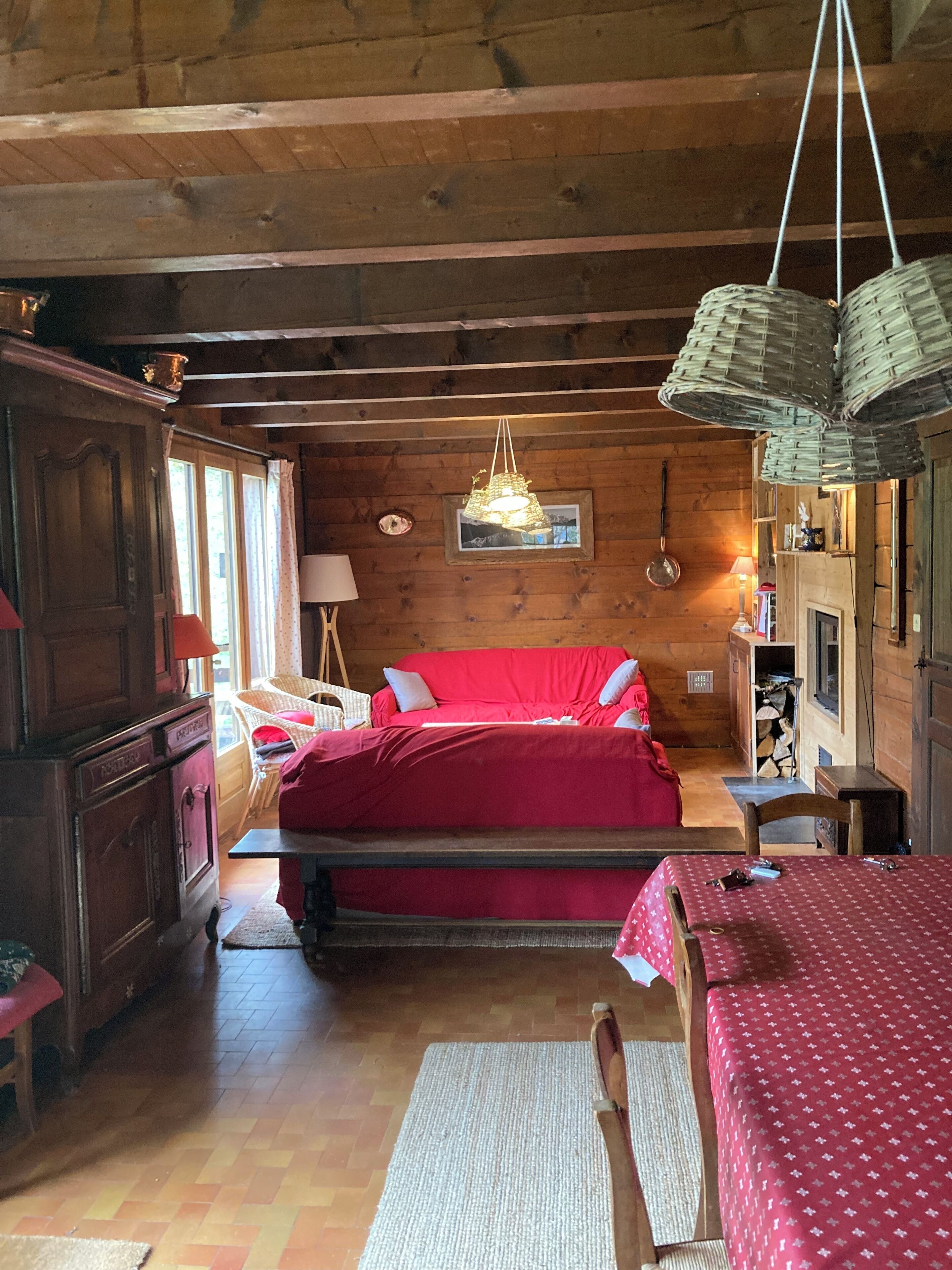 Une pièce chaleureuse avec un plafond en bois, un lit rouge, un luminaire suspendu en osier et une cheminée.