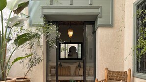 A cozy indoor seating area with a sofa and a wooden chair, a glass door leading to a room with a bed, and potted plants around. - Romantic Private Little Riad in Heart of Marrakech Medina (Marrakesh)