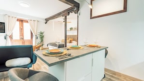A modern kitchen with a central island, a dining area with a sofa and chairs, and a wooden ceiling structure.