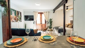 A dining area with a table set for two, a sofa, and a television in the background.