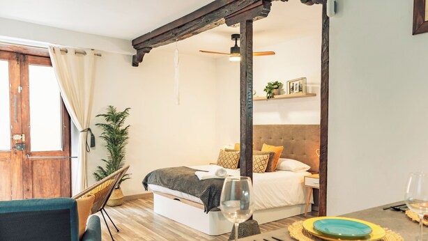 A bedroom with a bed, bedside table, and a view of the living area.