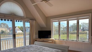 Un dormitorio con cama, televisión y ventanas amplias que ofrecen vistas del barrio.