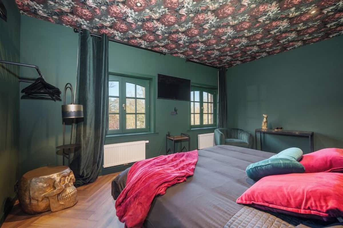 A room with a bed, a wooden sculpture, a radiator, a TV, and a window.