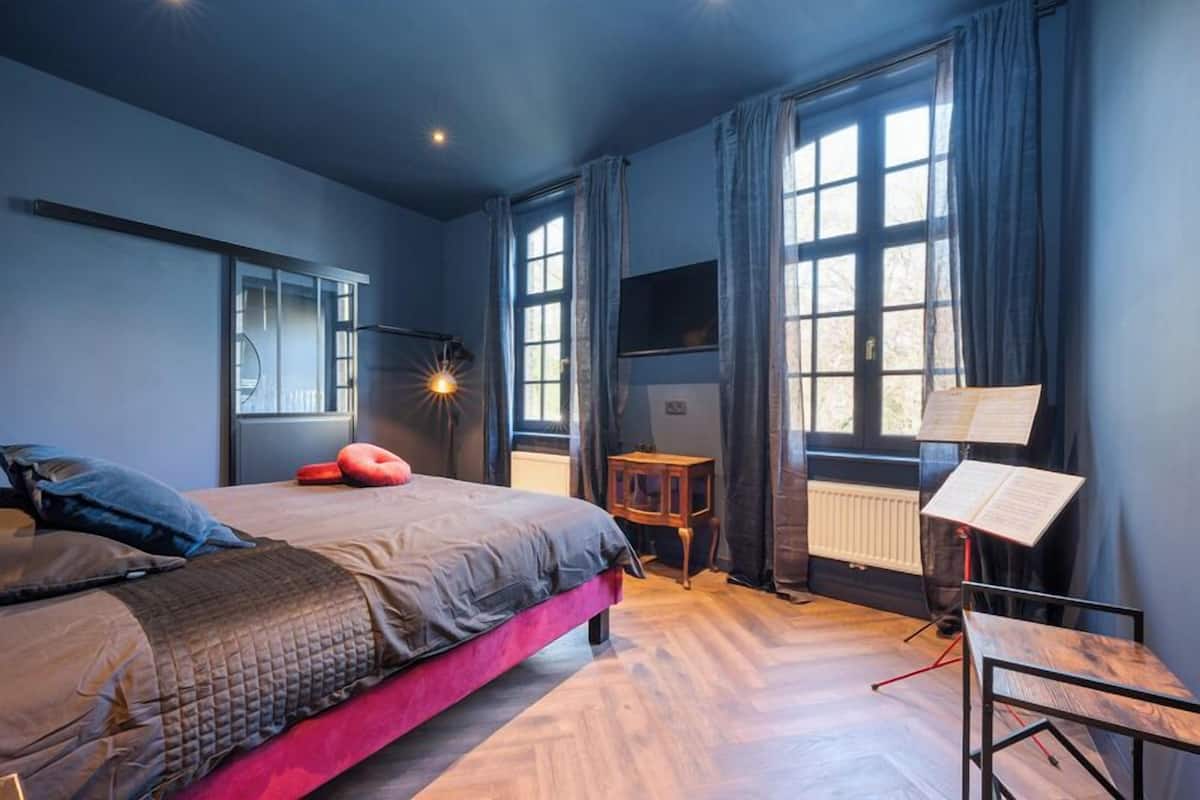 A bedroom with a bed, a TV, a music stand, and a window with curtains.