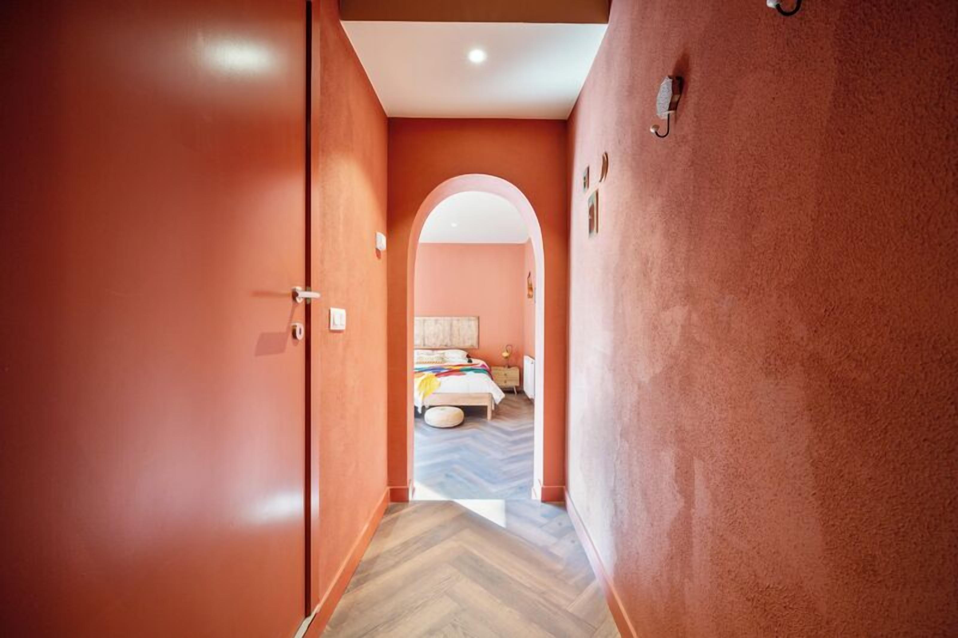 Een hal met een houten visgraatvloer die leidt naar een slaapkamer met een bed en een rond vloerkleed.