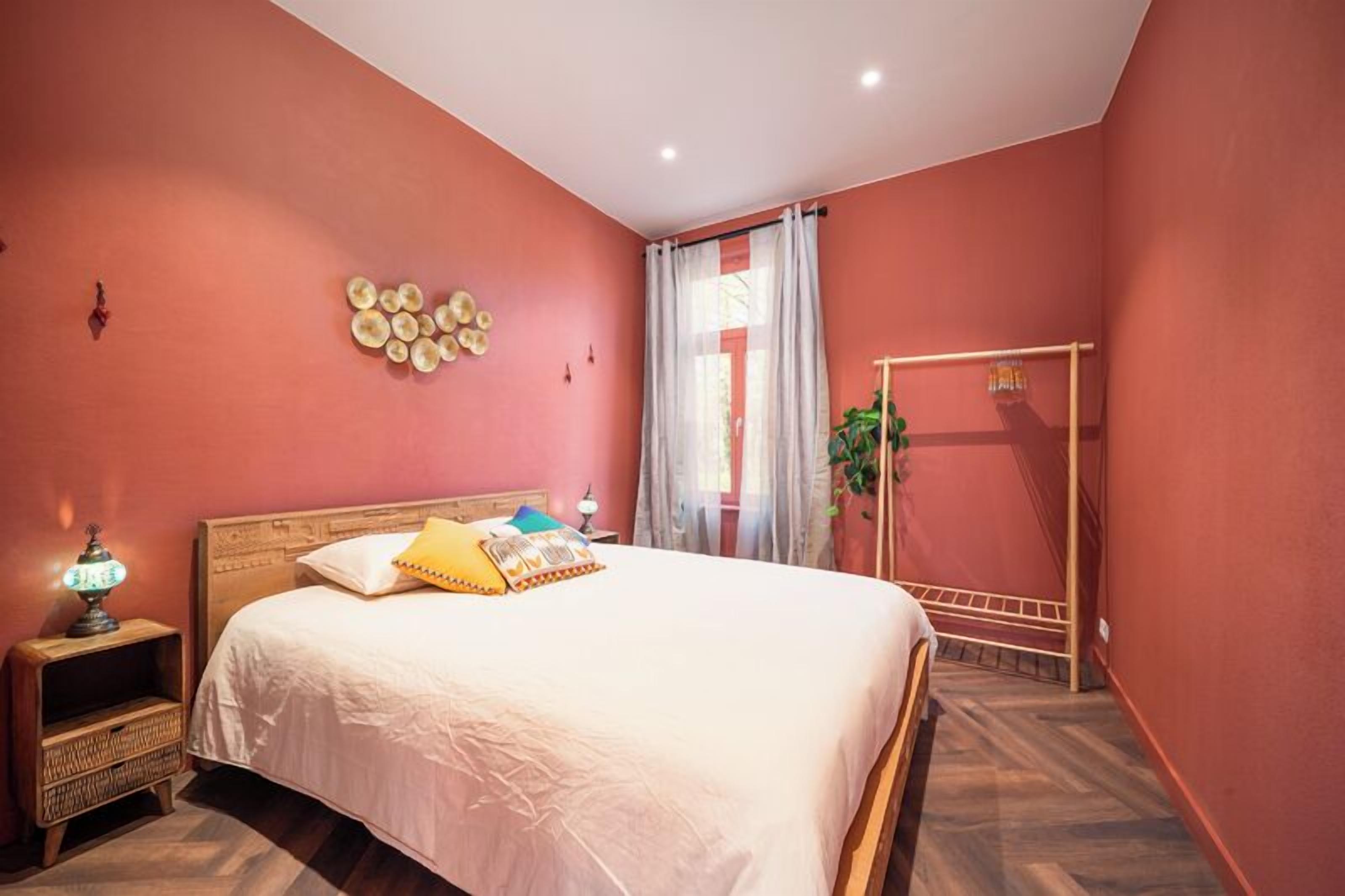 Une chambre à coucher avec un lit, une table de chevet, une horloge murale et une fenêtre avec des rideaux.