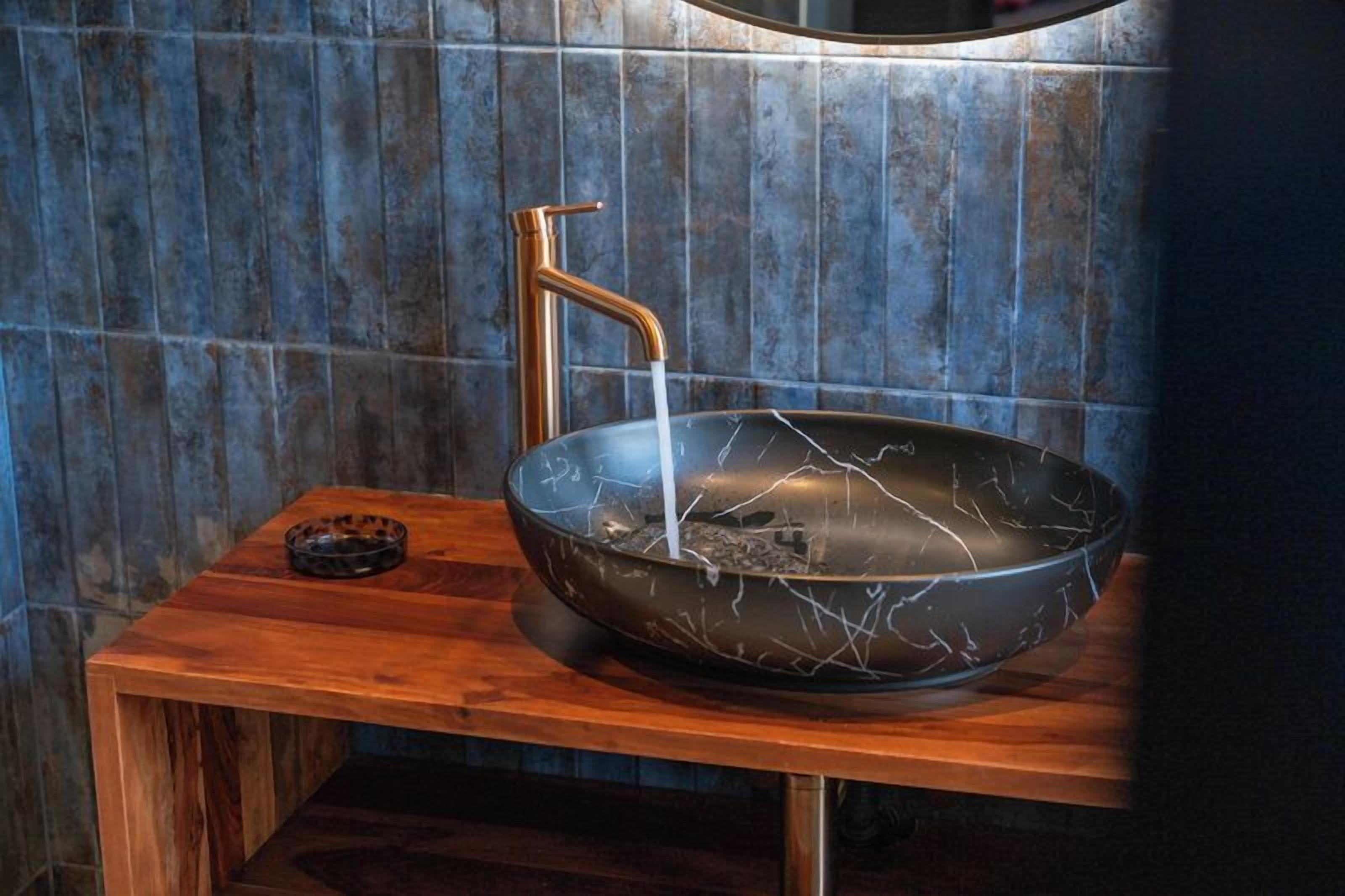 Un baño moderno con lavamanos de mármol, grifo de cobre y tocador de madera.