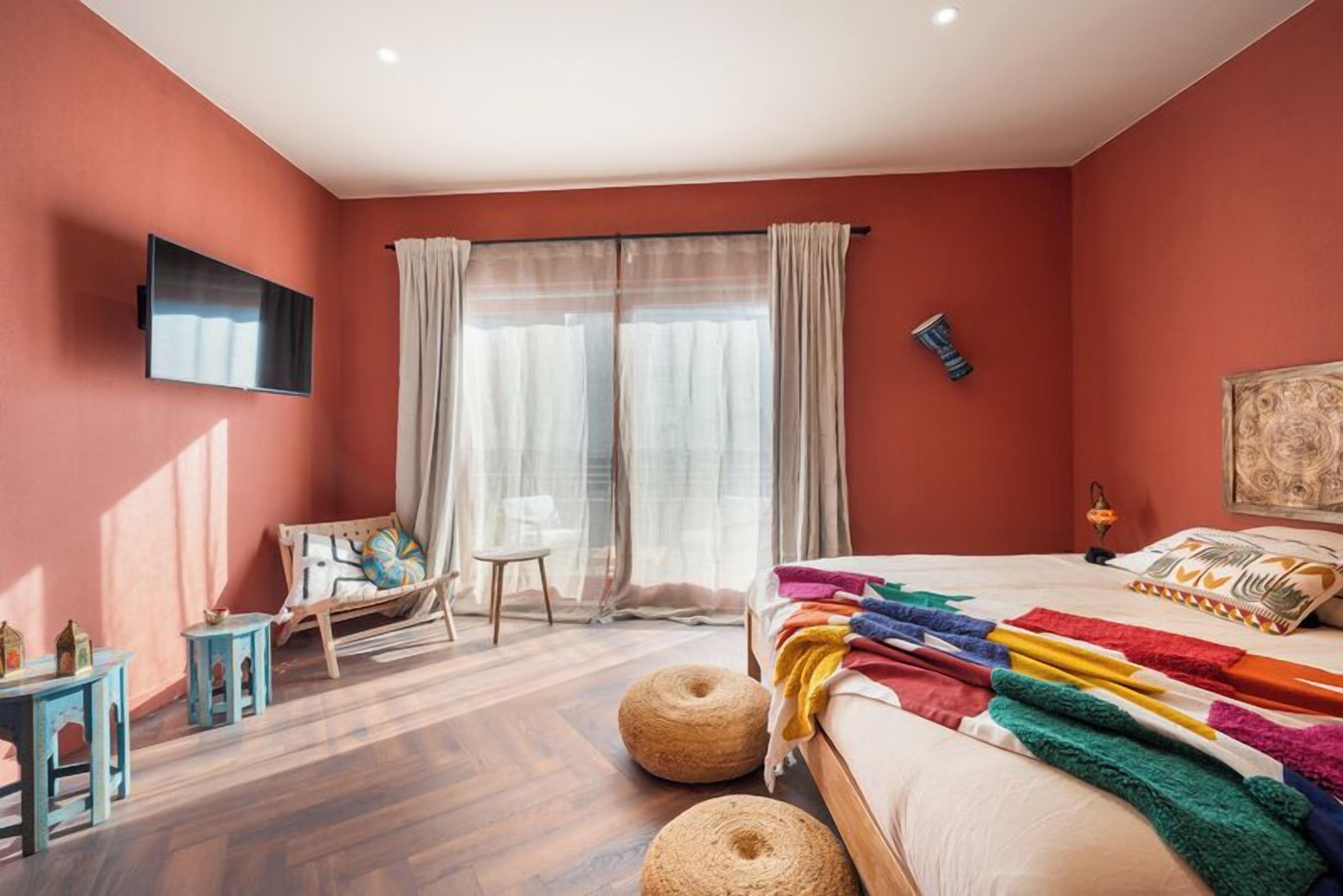 A bedroom with a bed, a TV, a chair, a small table, and a window with curtains.