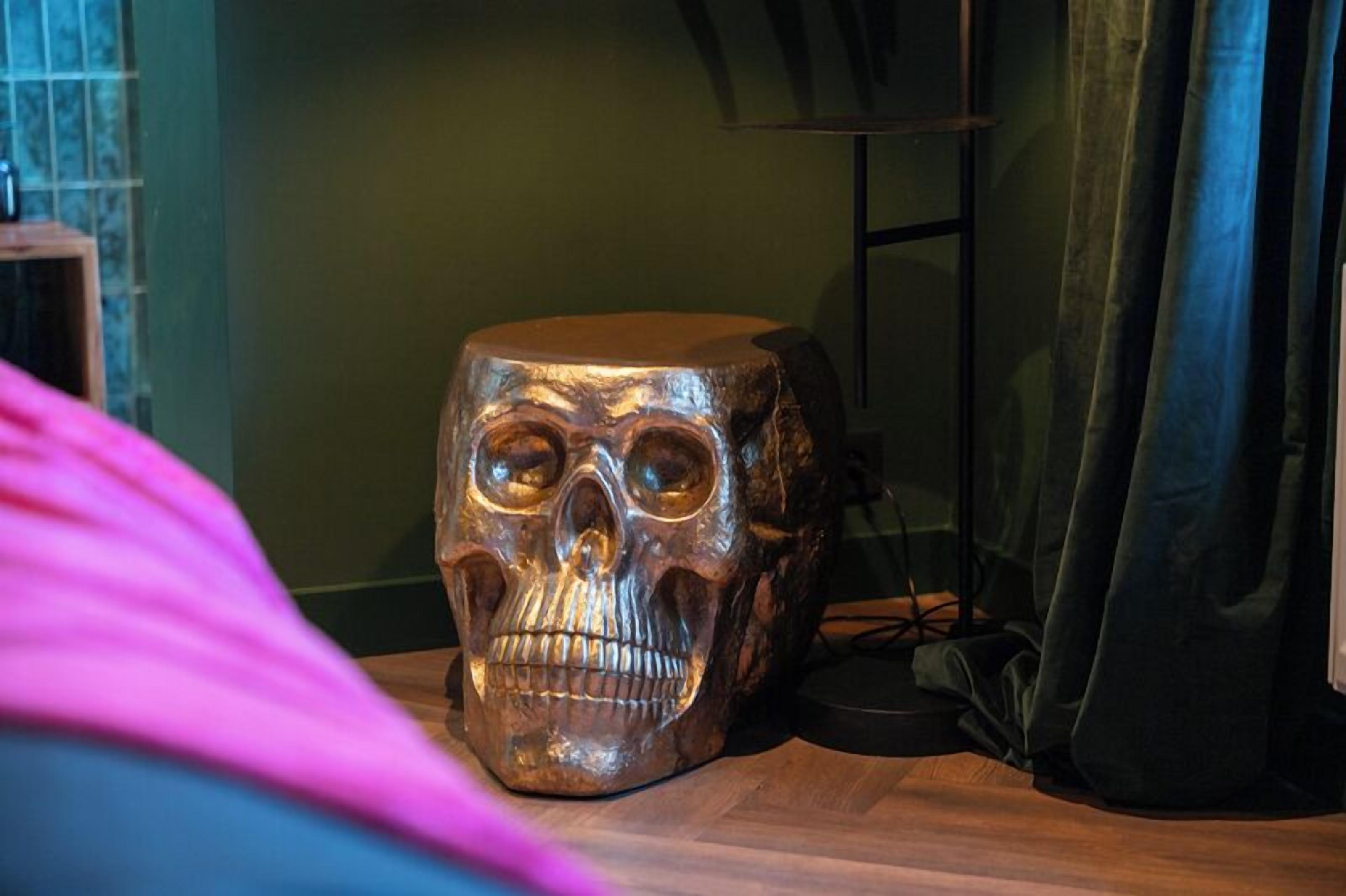 A wooden skull sculpture on a table in a room with a green wall and a black curtain.
