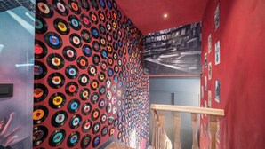 Un escalier avec un mur décoré de disques vinyles colorés, une main courante en bois et un mur rouge orné d’affiches.