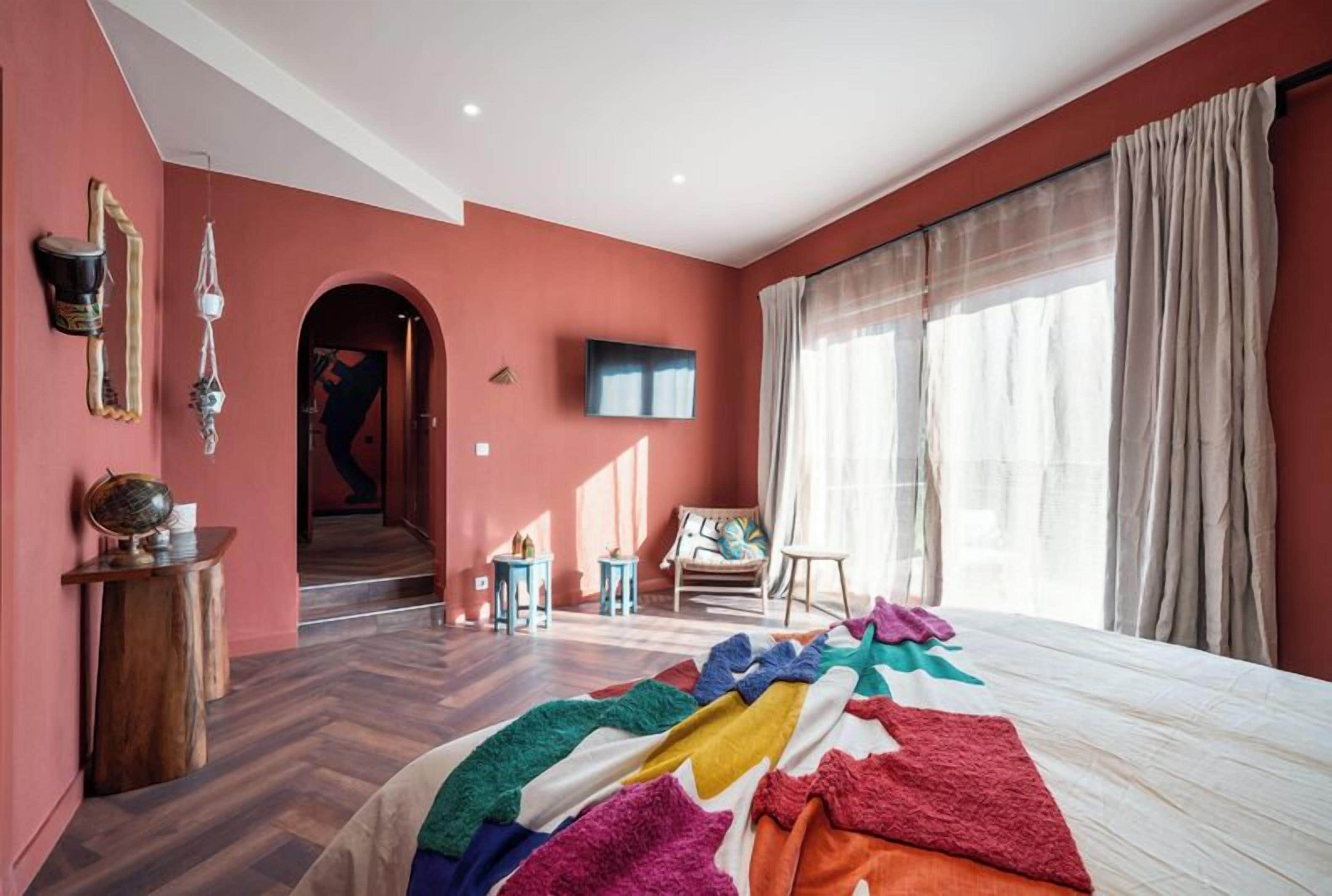 A bedroom with a large bed, a TV mounted on the wall, and a window with curtains.