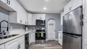 A modern kitchen with white cabinets, stainless steel appliances, and a wooden floor.