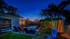 A backyard with a swimming pool, lounge chairs, and a house with a garage.