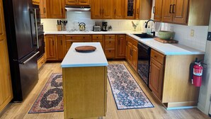 A modern kitchen with wooden cabinets, a black refrigerator, a central island, and a patterned rug. - Secluded, elegant country home only 10 minutes from Downtown Ithaca! (Ithaca)