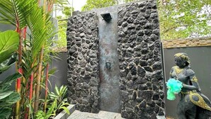 Un muro de piedra con una puerta metálica y una estatua de una figura sosteniendo un objeto azul.