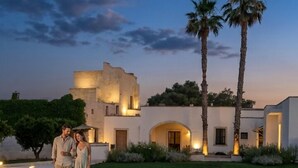 A poolside scene with a building, palm trees, and a clear sky. - Masseria Luci Grande (Scorrano)