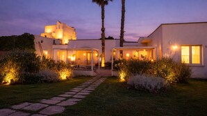 A modern house with a paved pathway leading to the entrance, surrounded by well-maintained bushes and palm trees. - Masseria Luci Grande (Scorrano)