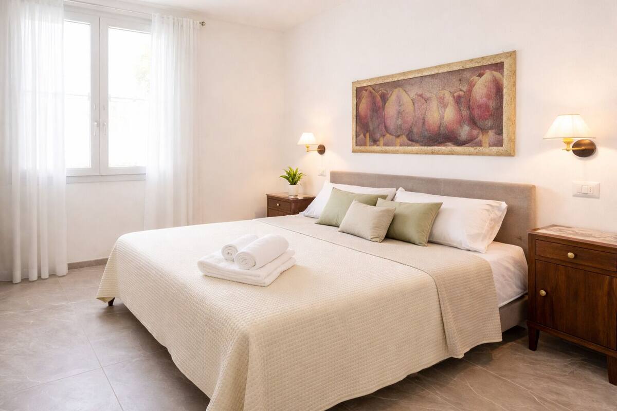 A hotel room with a large bed, a painting on the wall, two bedside lamps, and a window with curtains.
