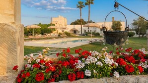 A pool area with lounge chairs, a hanging bucket, and a building with a white facade. - Masseria Luci Grande (Scorrano)