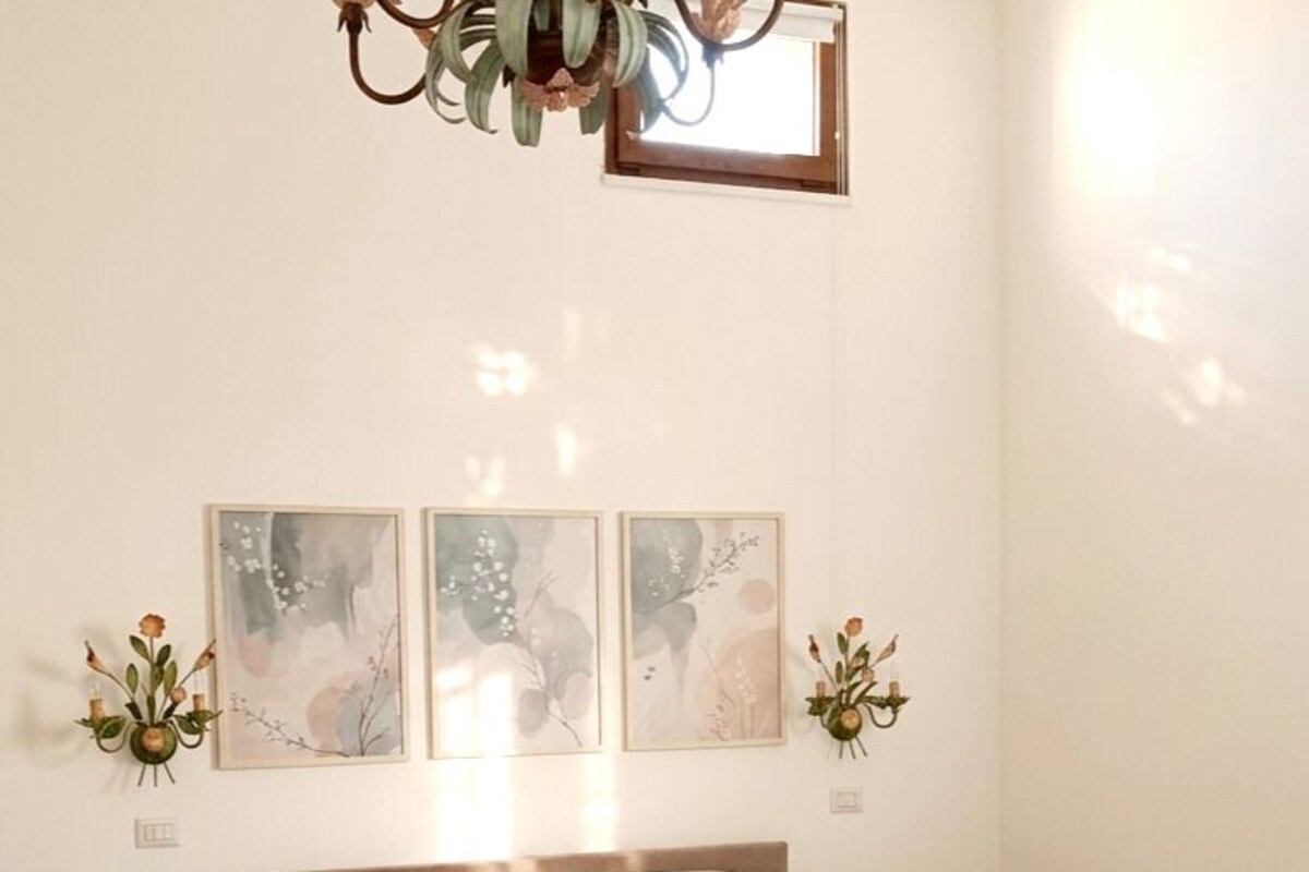 A bedroom with a large bed, two bedside tables, a chandelier, and three framed artworks on the wall.