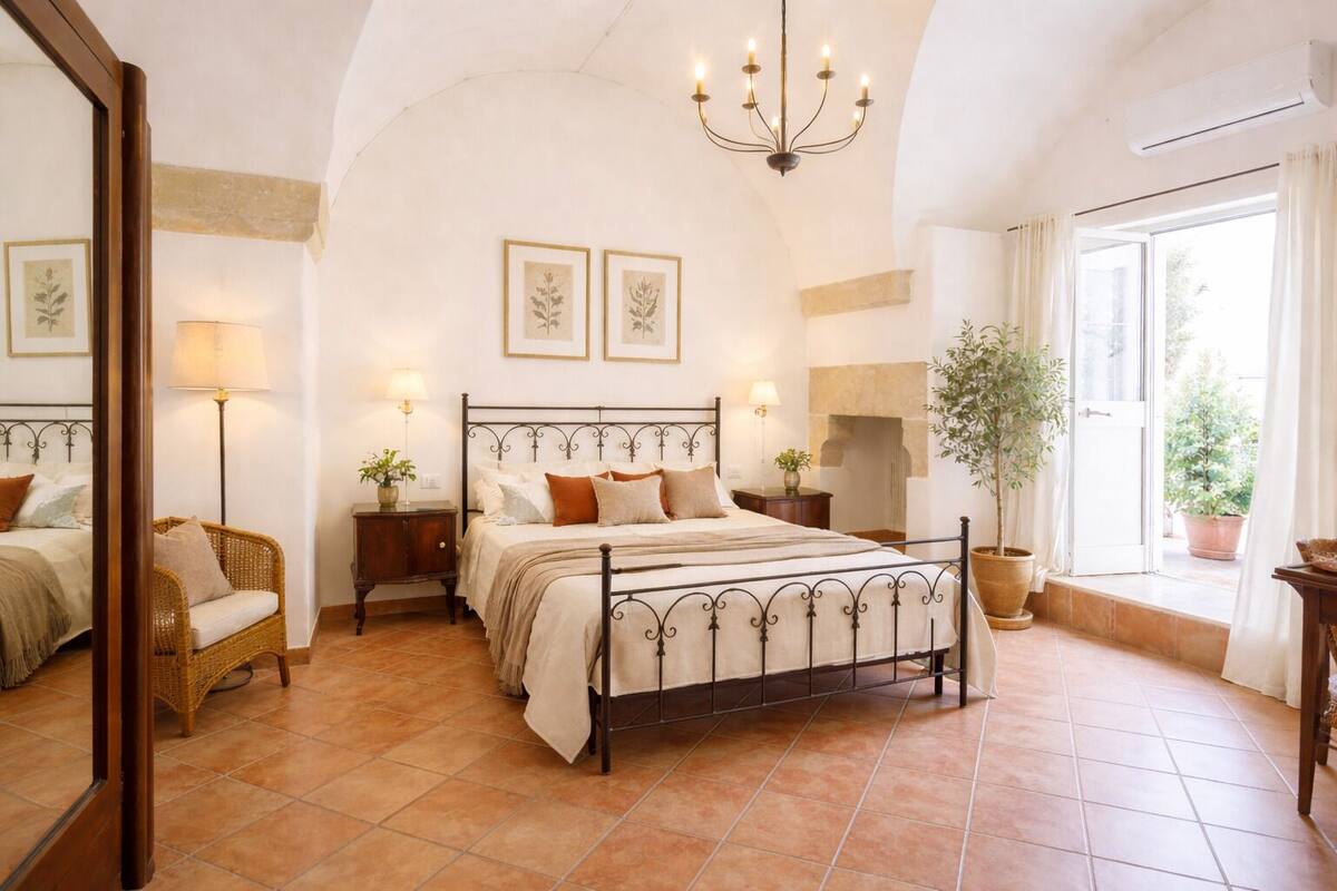 A bedroom with a bed, bedside tables, a chair, a chandelier, and a window with curtains.