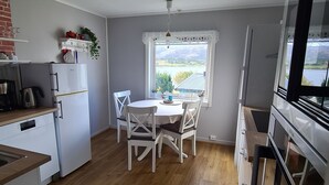 A compact kitchen with a dining area, a refrigerator, a stove, and a window with a view of mountains. - Cozy vacation apartment in central Norway with mountains and sea on your doorstep (Trøndelag)