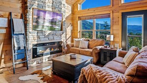 A cozy living room with a stone fireplace, leather sofas, and large windows offering mountain views. - Ridgetop Retreat - Epic Views - Hot Tub - Fire Pit - Kid Friendly - Arcade (Sevierville)