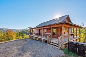 Une cabane en bois avec un porche, une allée en gravier et une vue sur les montagnes en arrière-plan.