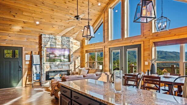 A spacious living area with a stone fireplace, large windows, and a high ceiling with wooden beams. - Ridgetop Retreat - Epic Views - Hot Tub - Fire Pit - Kid Friendly - Arcade (Sevierville)