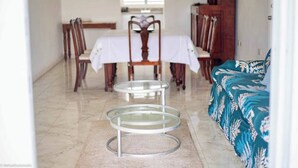 Un coin repas avec une table dressée pour quatre personnes, une table basse en verre à trois niveaux et un canapé recouvert d’un tissu à motifs floraux.