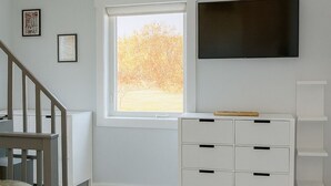 Ein Zimmer mit einem weißen Kommode, einem an der Wand montierten Fernseher und einem Fenster mit Blick auf Bäume.