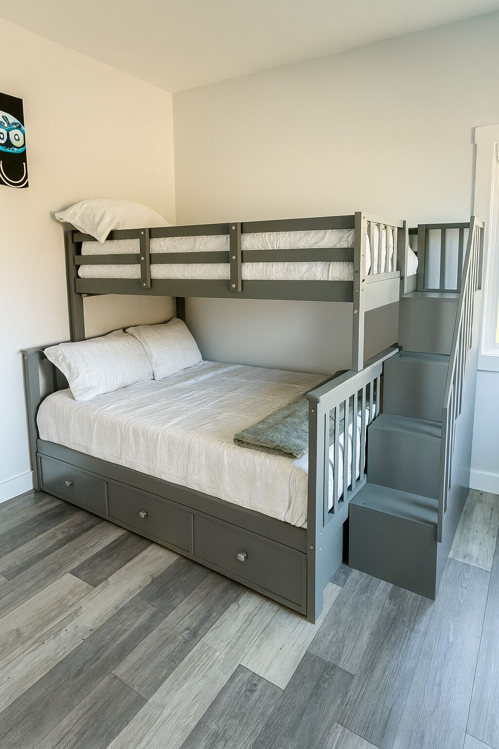 Un lit superposé avec un lit inférieur et un bureau escamotable, une structure en bois grise et un matelas blanc.