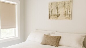 Ein ordentlich bezogenes Bett mit einer beige farbenen Decke, weißen Kissen und einem Baumgemälde an der Wand.