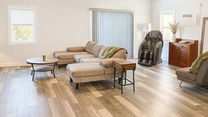 Ein geräumiges Wohnzimmer mit einer großen, im L-förmigen Winkel angeordneten Couch, einem runden Couchtisch und einem Ledersessel.