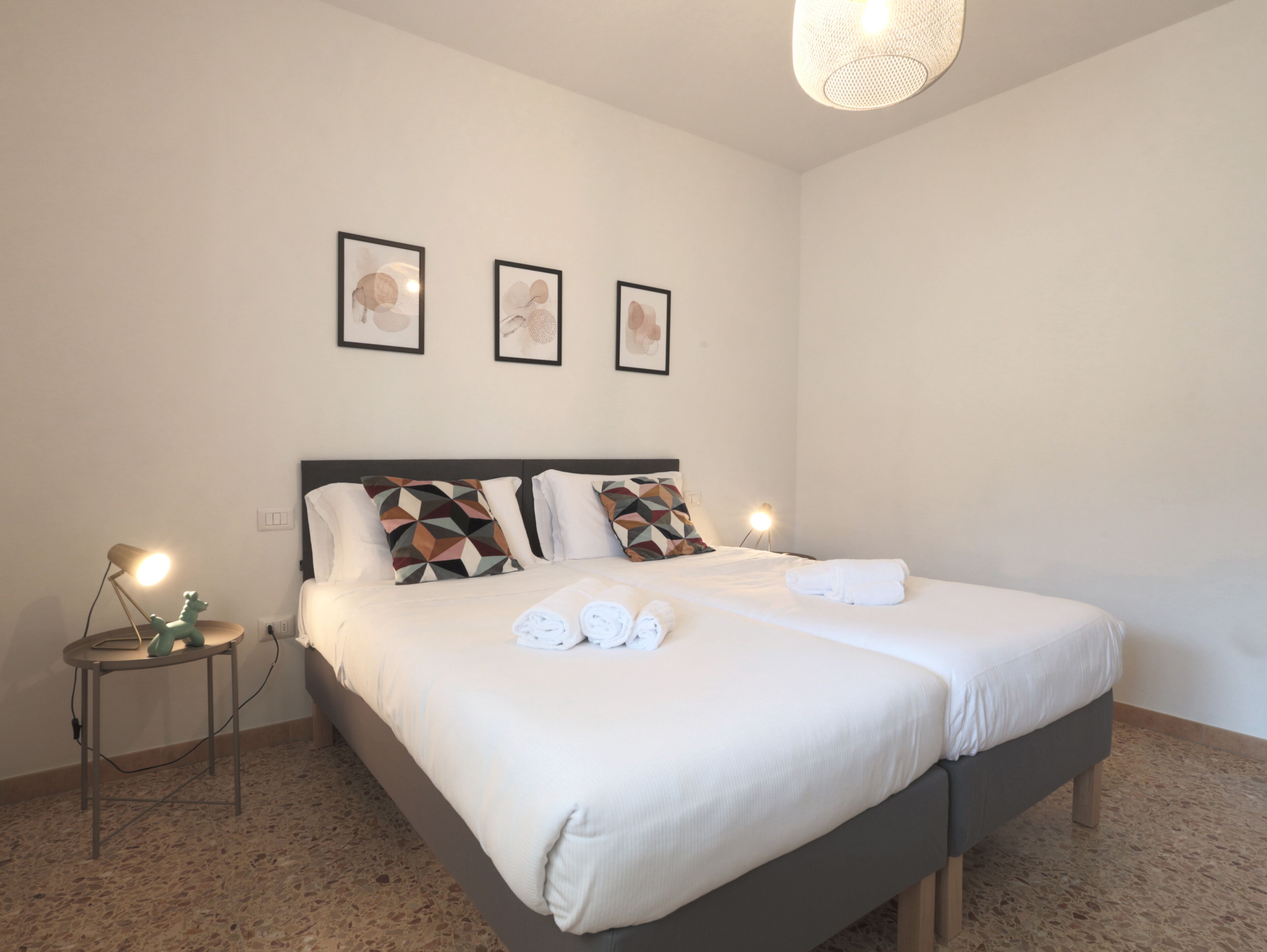 A neatly made double bed with pillows, a bedside table with a lamp, and three framed pictures on the wall.