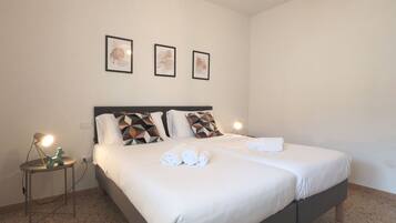 A neatly made double bed with pillows, a bedside table with a lamp, and three framed pictures on the wall.