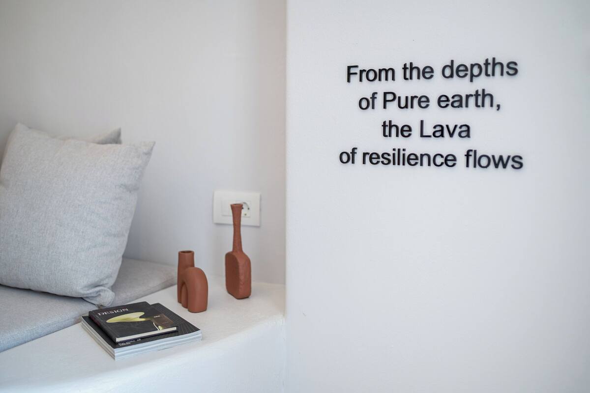 A minimalist room with a white wall, a grey pillow, two brown vases, and a book on a white surface.