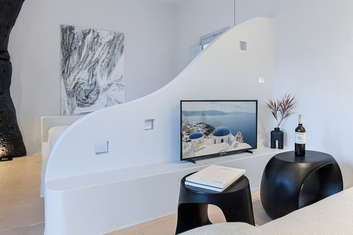 A modern living room with a curved white wall, a flat-screen TV, a book, and a bottle of wine on a black side table.