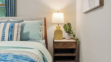 A neatly made bed with a blue and white striped pillow, a bedside lamp, and a small wooden nightstand with a plant.