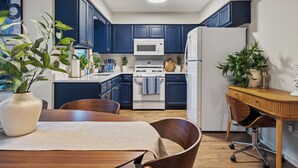 A compact kitchen with dark blue cabinets, a white refrigerator, a microwave, and a stove. There are two wooden chairs and a small wooden table. - Spacious 4BR Home Family & Pet-Friendly  2 Living Rooms + Game Fun in Plainfield (Plainfield)