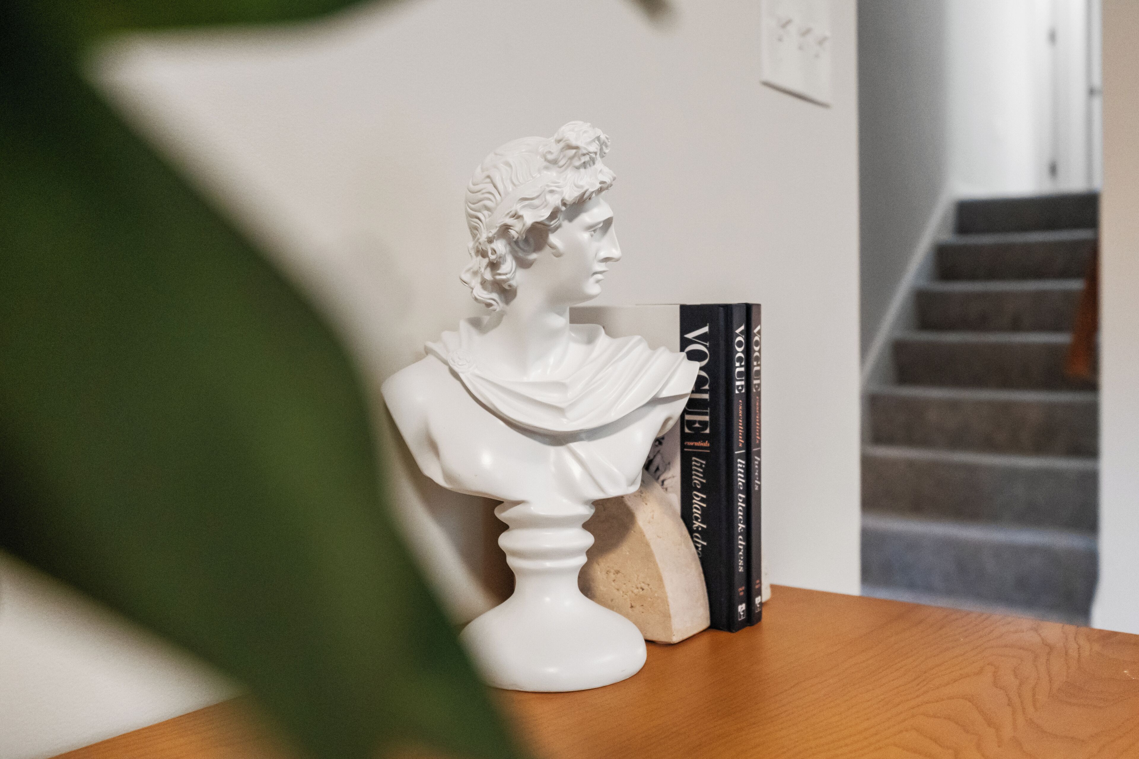 Een borstbeeld op een houten tafel, met boeken ernaast.