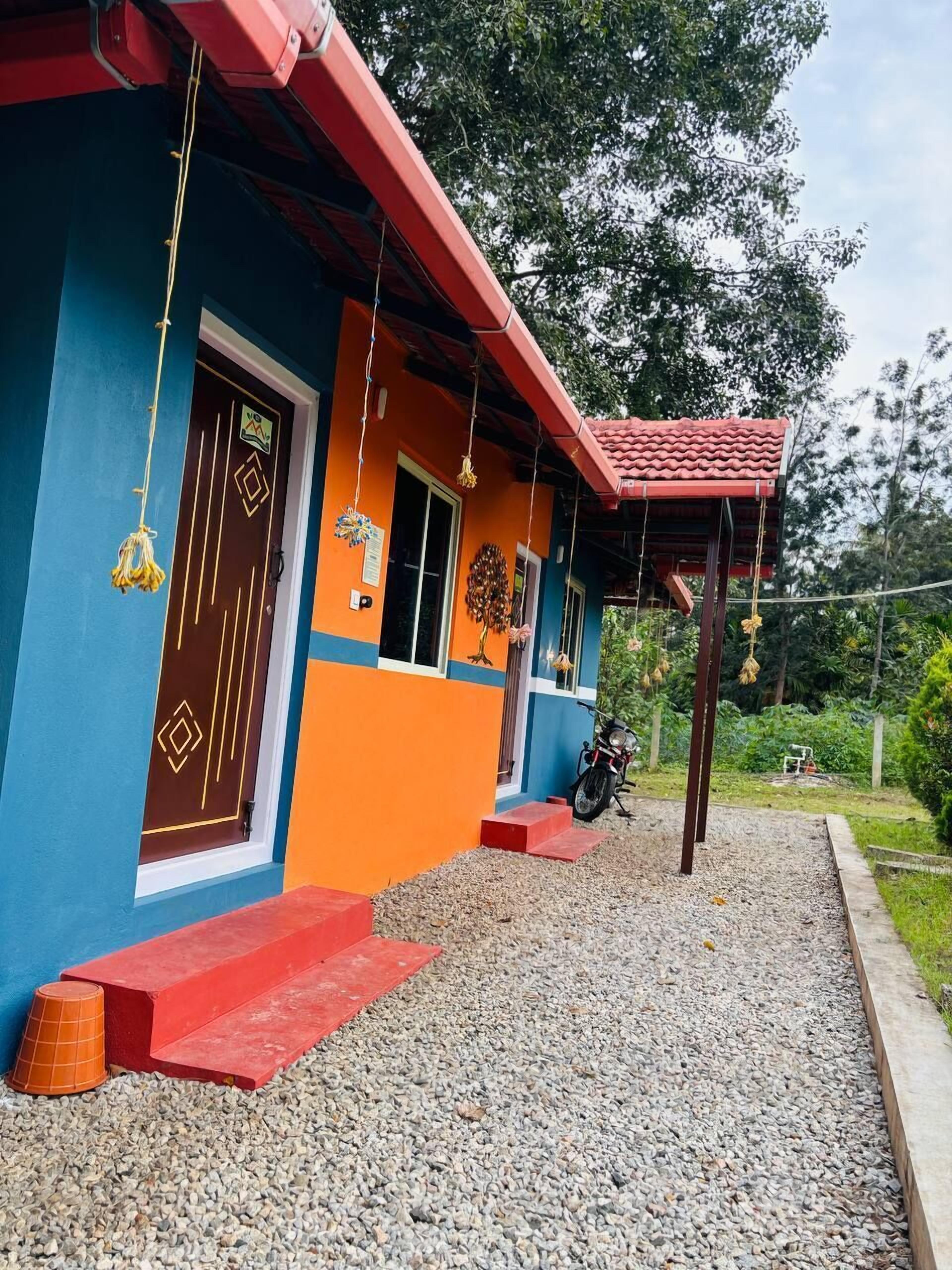 Une maison aux couleurs vives, avec un toit rouge, une moto garée devant et une allée gravillonnée.
