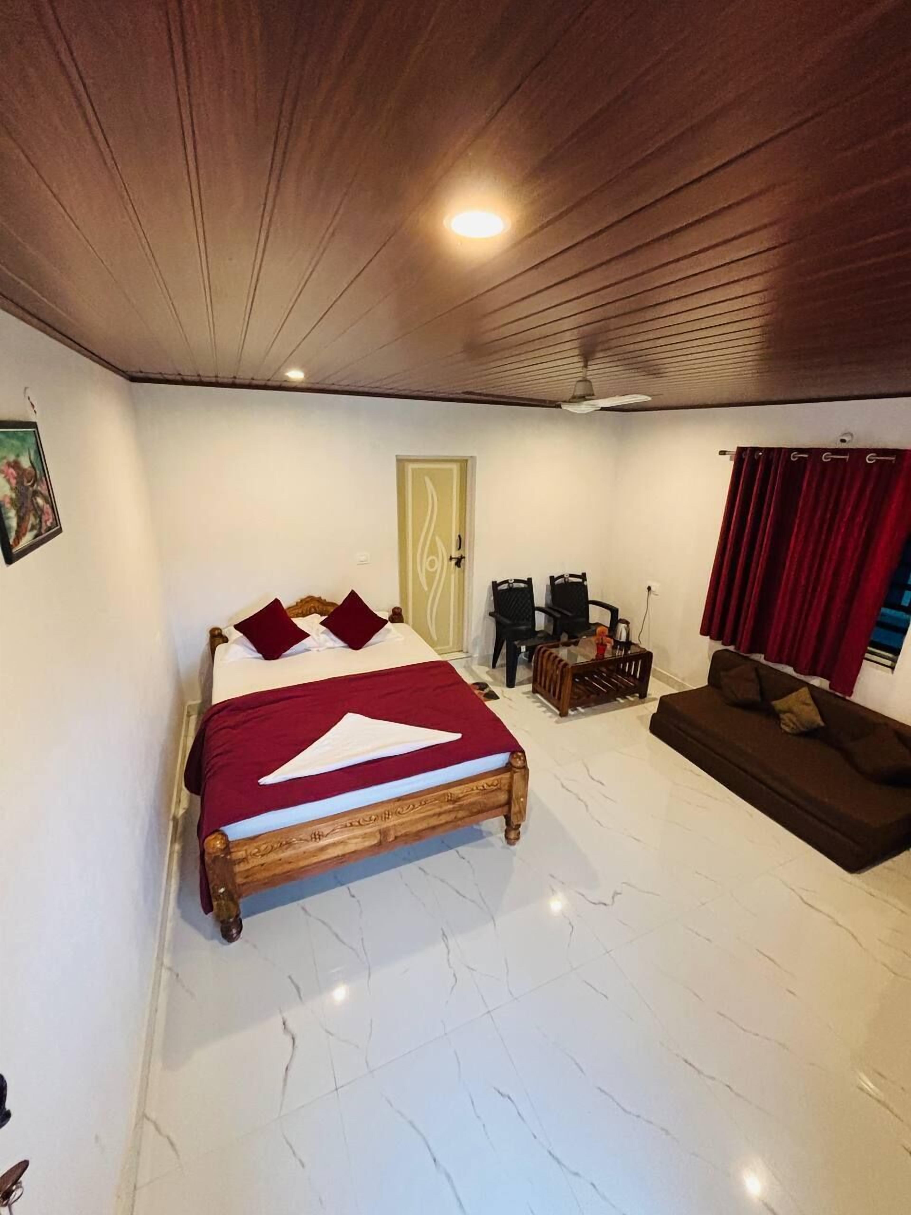 A bedroom with a bed, a sofa, a wooden ceiling, and a door.