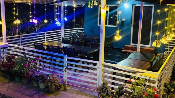 An outdoor patio area with a covered seating area, string lights, and potted plants. - COORG SUNRISE COTTAGES (Kushalnagar)