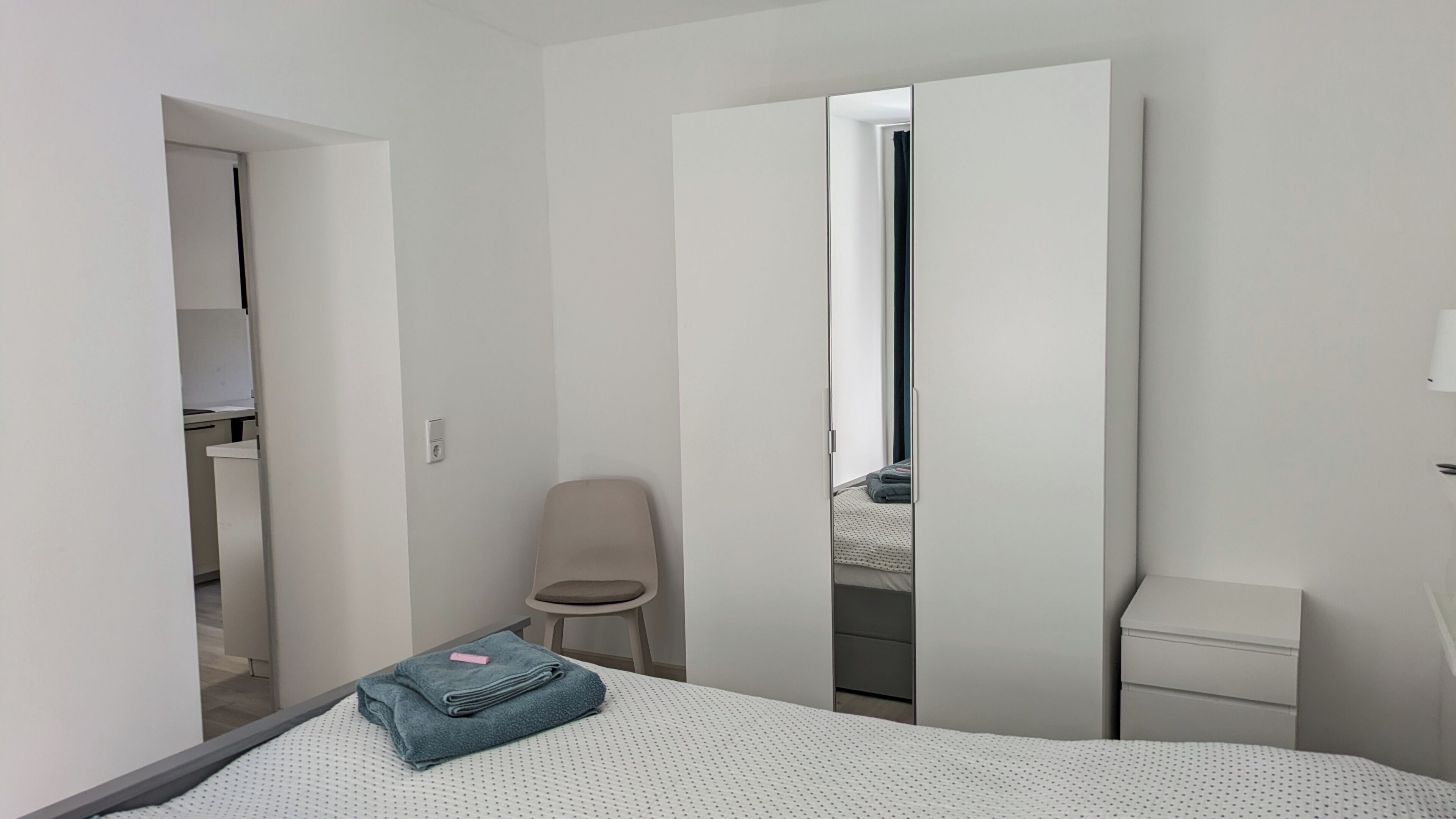 Een slaapkamer met een bed, een stoel, een kledingkast en een nachtkastje.