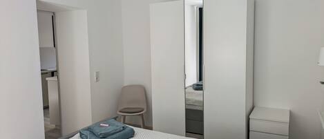 Een slaapkamer met een bed, een stoel, een kledingkast en een nachtkastje.