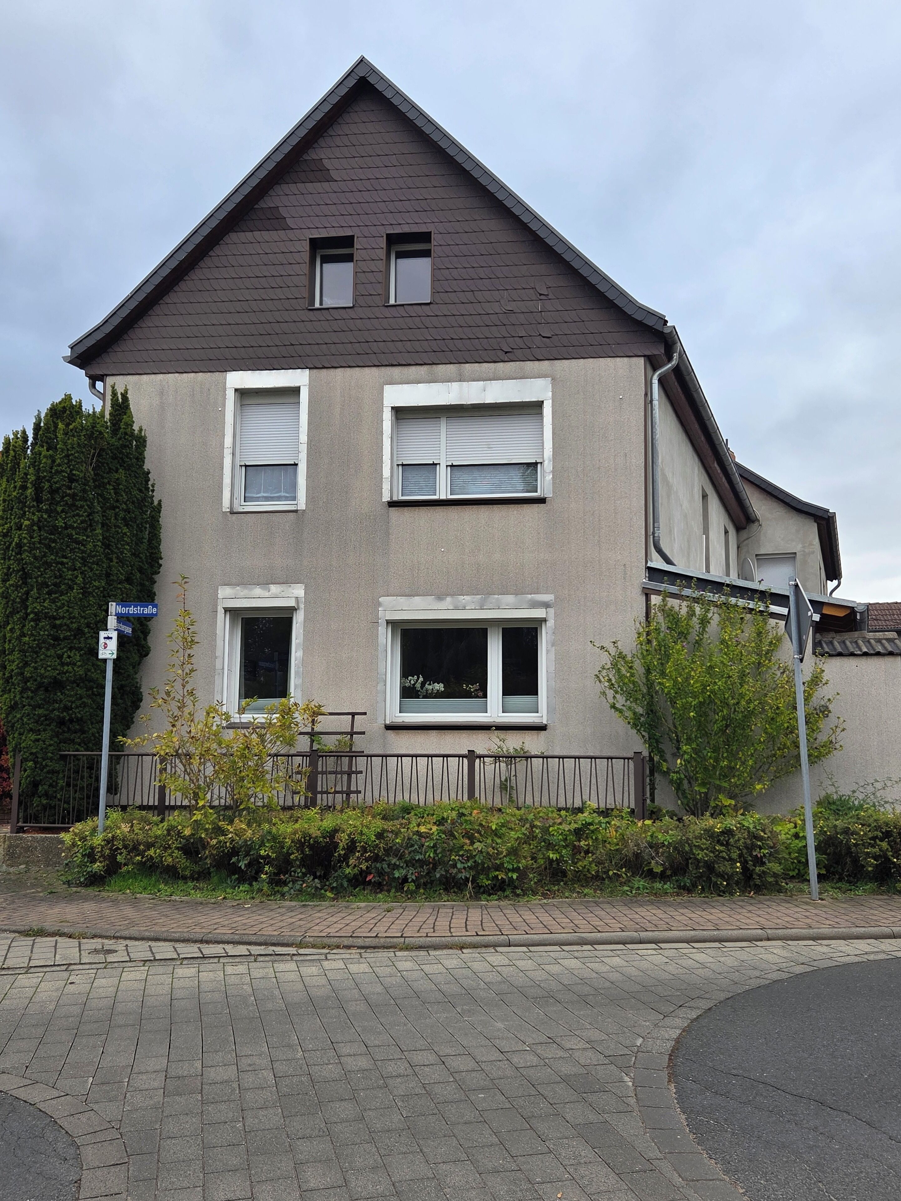 Een woonhuis met twee verdiepingen, een grijze gevel, twee ramen op de bovenverdieping en een klein balkon.