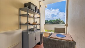 A balcony with wicker furniture, a metal shelf unit with hats and baskets, and a view of trees and sky.