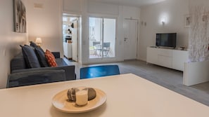A modern living room with a sofa, a dining table with a candle, and a TV.