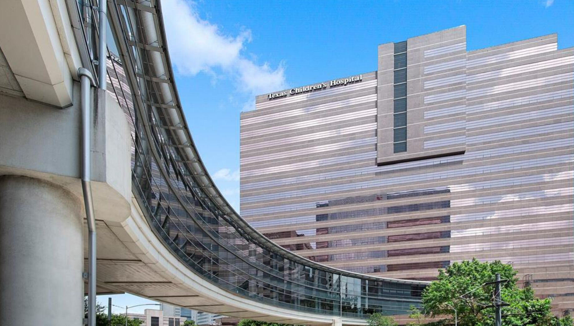 Un bâtiment moderne doté d’une passerelle vitrée incurvée et portant l’inscription « Texas Children’s Hospital » sur sa façade.